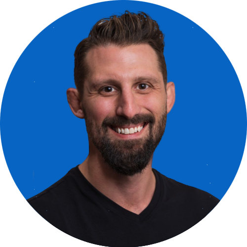 Smiling man with dark hair and beard, wearing a black shirt, against a solid blue background.